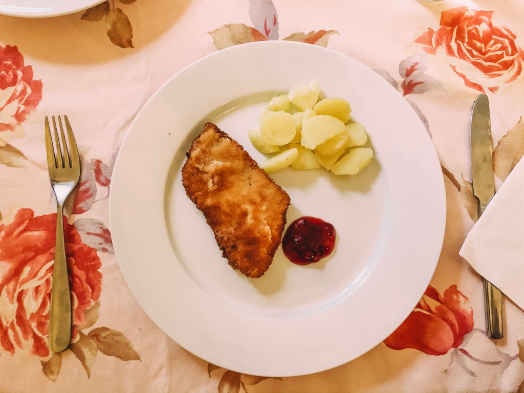 chicken schnitzel on a plate with potato salad and lingonberry sauce